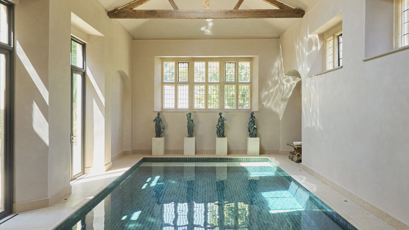 The indoor pool at Ampney Park, lined in Foundry Porcelain Smeraldo tiles with a Buscot Limestone surround, beneath exposed timber trusses
