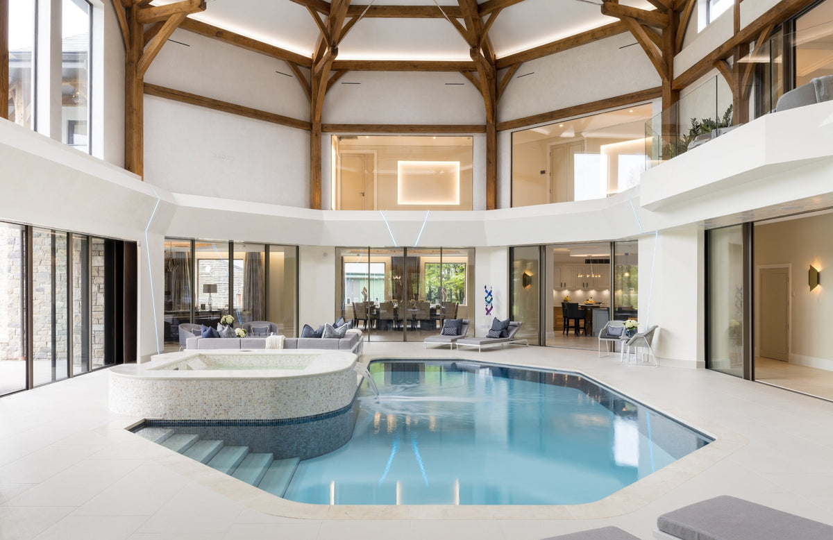 Double-height indoor pool hall with oak trusses, mosaic spa and pale limestone surround