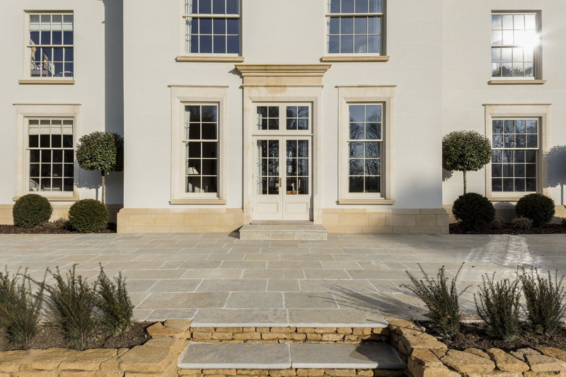 Rendered country house facade with stone window surrounds, above a limestone paved terrace and stone steps