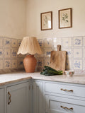 Aesop's Fables Pottery Blue tile splashback in a kitchen with pale blue cabinetry, marble worktop and terracotta lamp