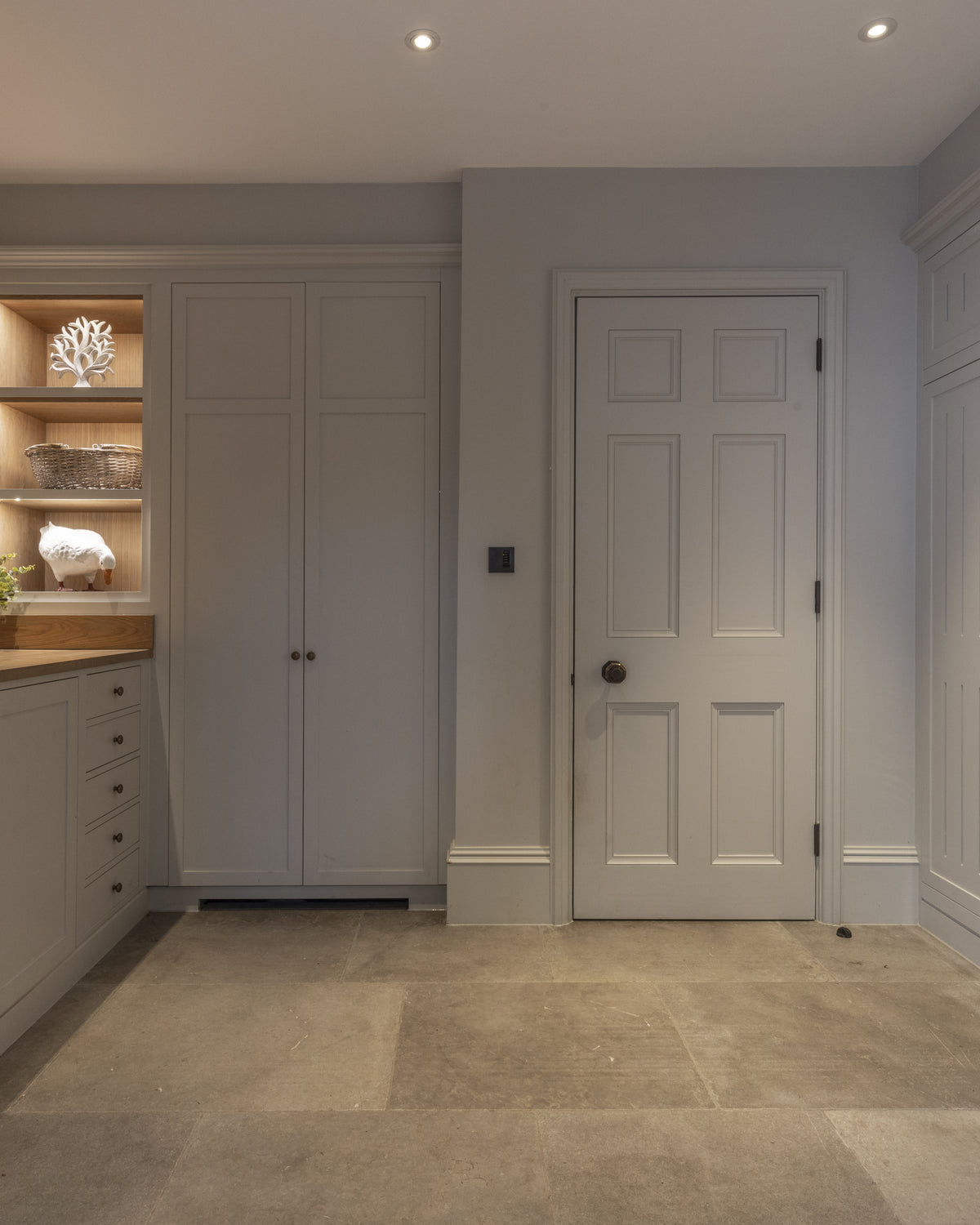 Amaya Limestone Tumbled Finish flagstone floor in a boot room and utility with pale grey joinery, a butler sink under a lit shelf niche and a coat nook with oak bench