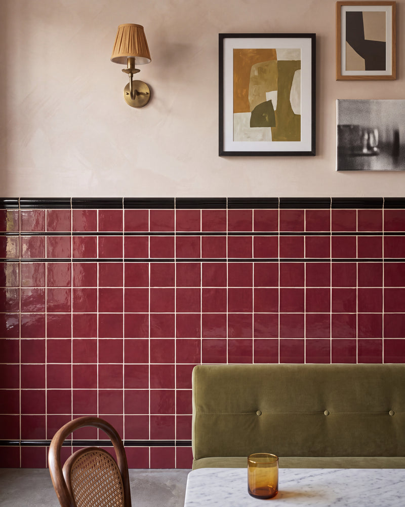 Architectural Mouldings Dado Ceramic Black capping a burgundy gloss square tiled wall in a restaurant booth, with black pencil banding and a black bead moulding below and a green velvet banquette