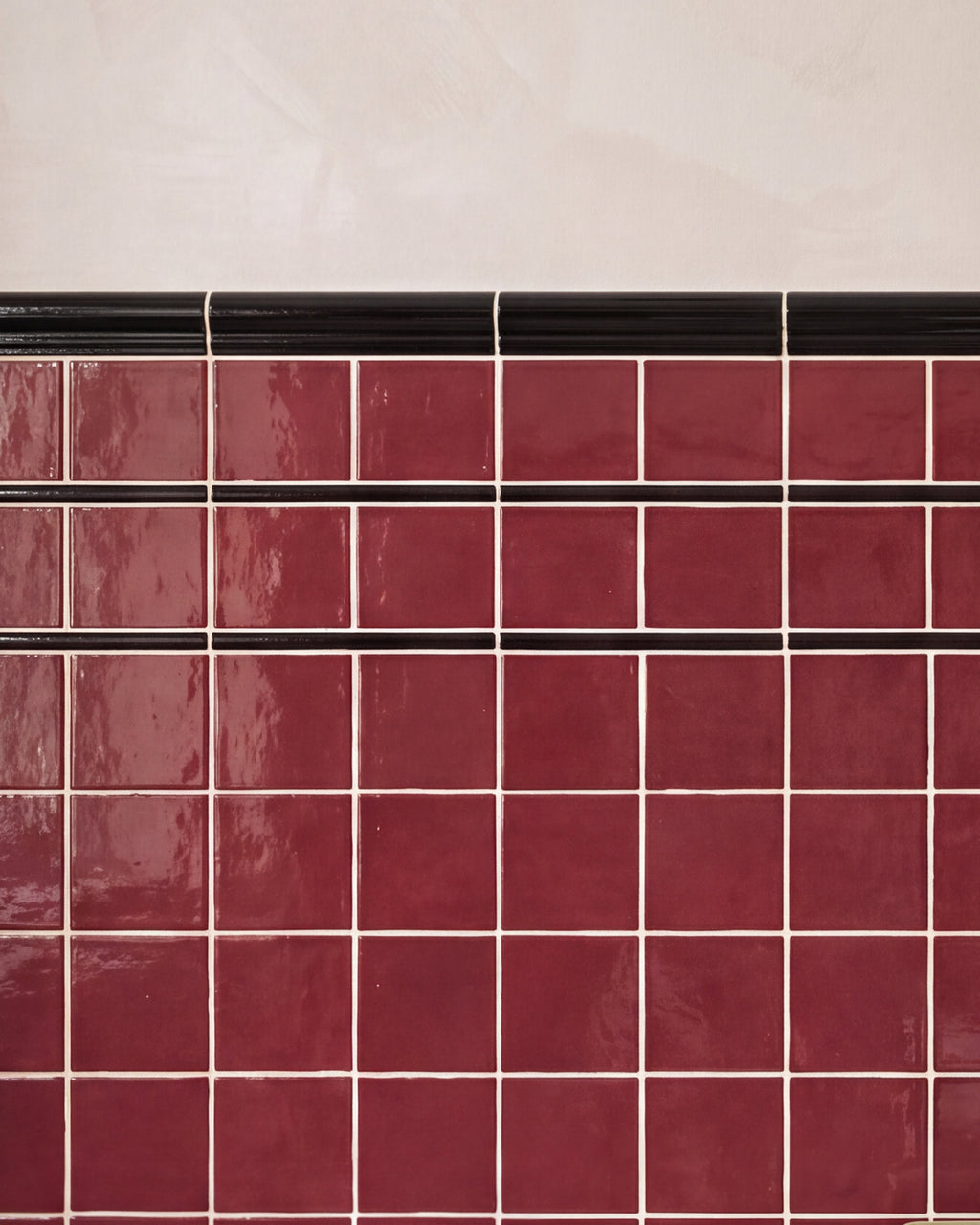 Close crop of Architectural Mouldings Dado Ceramic Black, the ribbed black rail finishing the top edge of a burgundy gloss square tiled wall against pink plaster