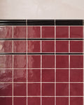 Close crop of two courses of Architectural Mouldings Pencil Ceramic Black banding a burgundy gloss square tiled wall beneath a black dado rail