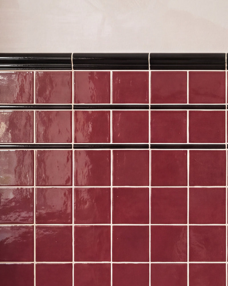Close crop of two courses of Architectural Mouldings Pencil Ceramic Black banding a burgundy gloss square tiled wall beneath a black dado rail