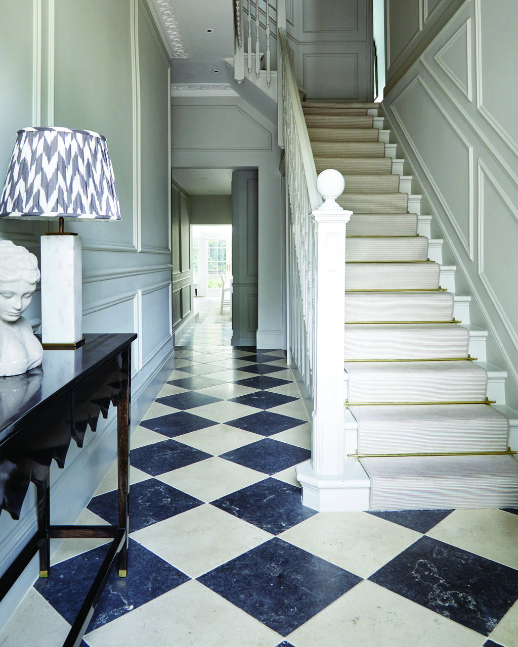 Bergamo Limestone Lightly Seasoned Finish in a chequerboard with Royal Mink Limestone running through a panelled stair hall with a runner and brass stair rods