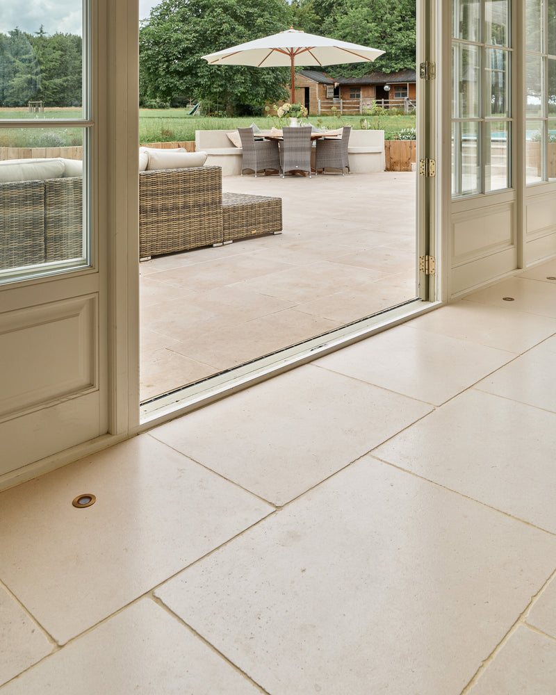 Blandford Limestone Tumbled Finish running from a garden room through open French doors onto a paved terrace with rattan seating and a parasol