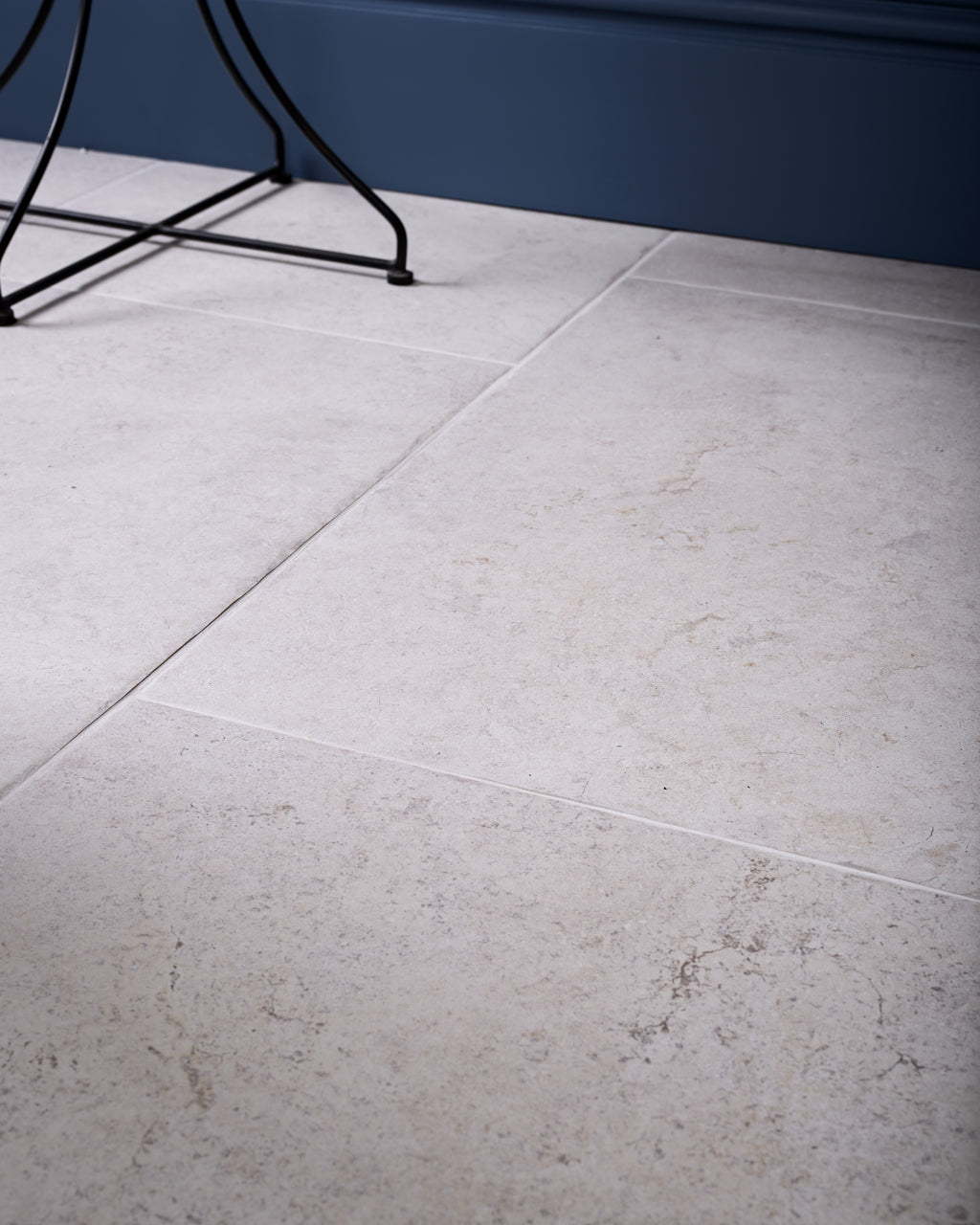 Brit Stone Minster Porcelain floor tiles laid in a large format against a deep blue skirting, with a slim black side table foot resting on the stone