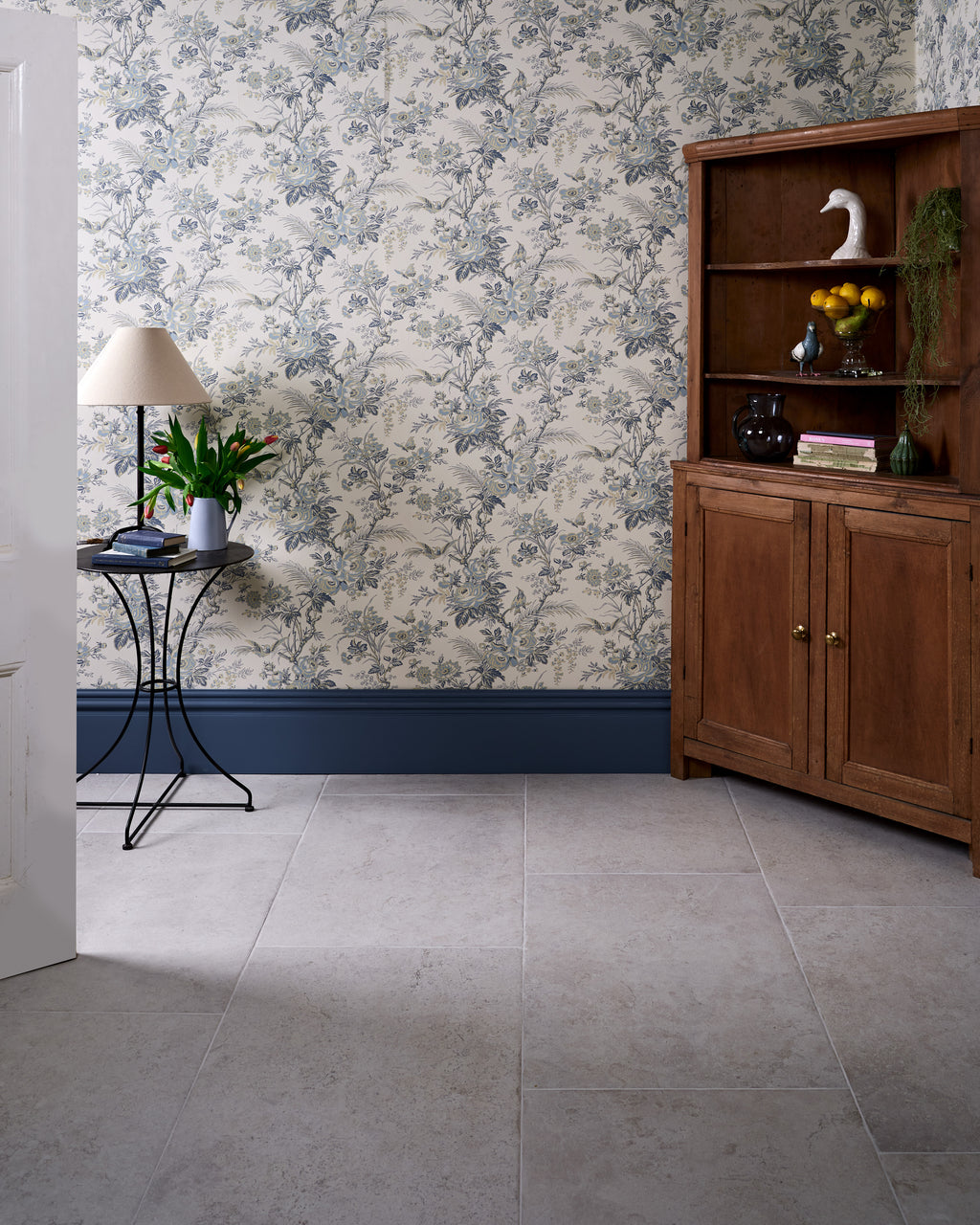 Brit Stone Minster Porcelain across a hallway floor, with blue and green floral wallpaper, deep blue skirting and an antique pine corner dresser