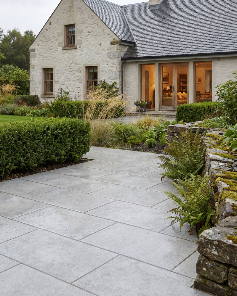 Brit Stone Pennant Porcelain Paving forming a wide path to a whitewashed stone cottage, edged by box hedging, grasses and a mossy dry stone wall with ferns
