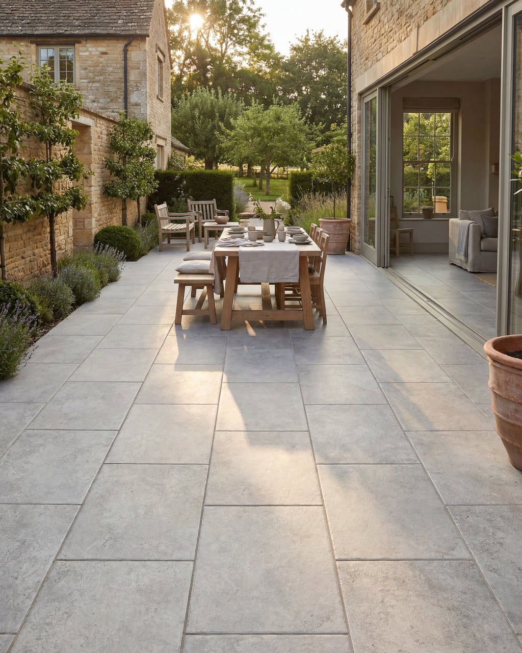 Brit Stone Pennant Porcelain Paving across a narrow courtyard between Cotswold stone buildings, with a laid oak dining table in low evening sun