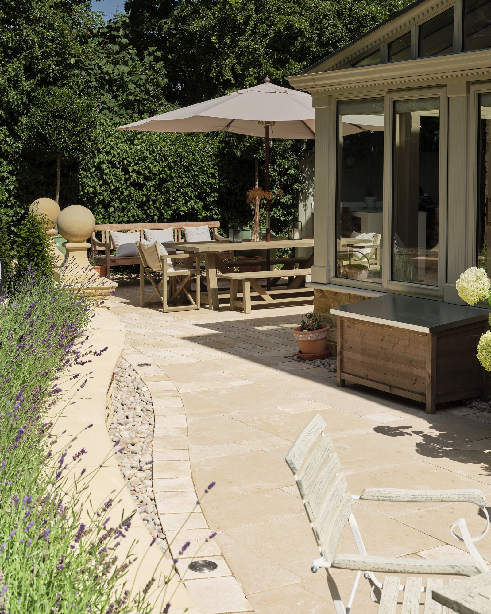 Buscot Limestone Cobble Tumbled & Etched Finish setts laid as a band through limestone paving on a sunny terrace outside a painted timber orangery