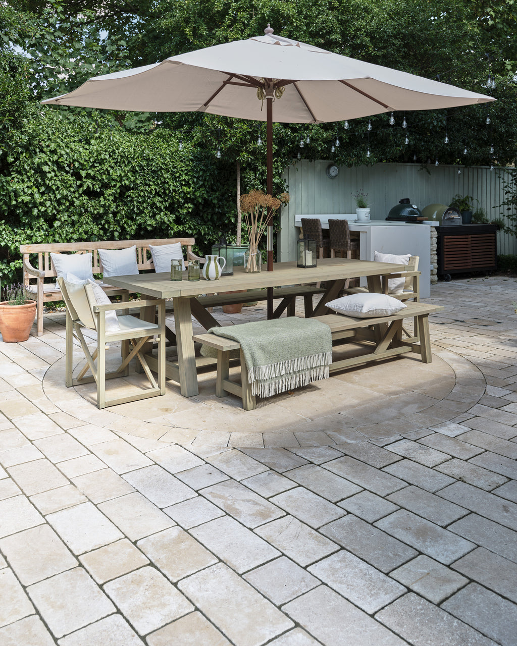Buscot Limestone Cobble Tumbled & Etched Finish laid around a circular paved feature under an outdoor dining table, parasol and festoon lights