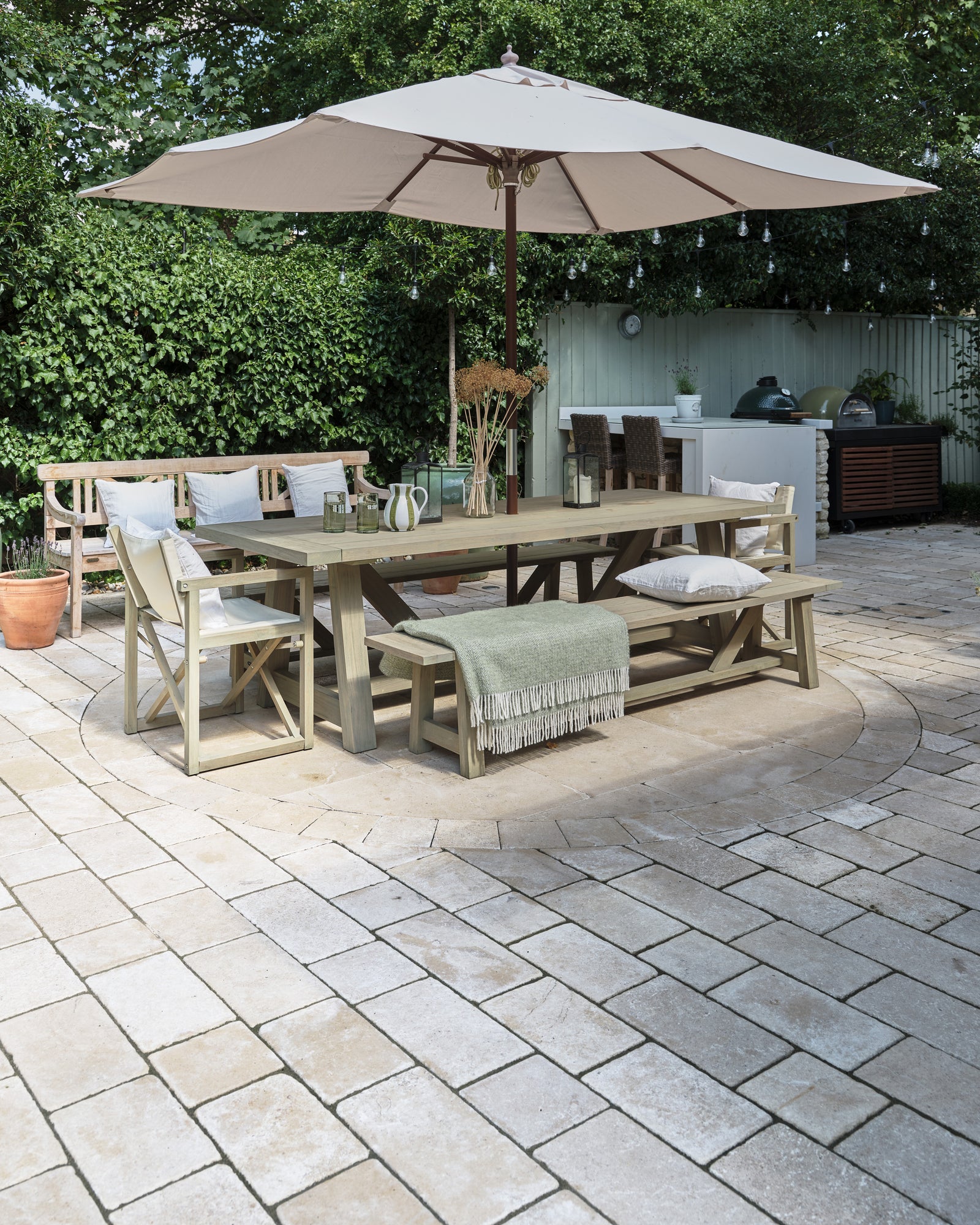 Buscot Limestone Cobble Tumbled & Etched Finish laid around a circular paved feature under an outdoor dining table, parasol and festoon lights