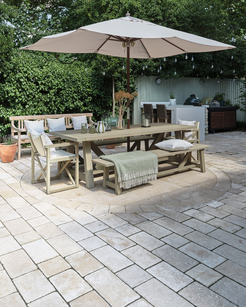 Buscot Limestone Cobble Tumbled & Etched Finish laid around a circular paved feature under an outdoor dining table, parasol and festoon lights
