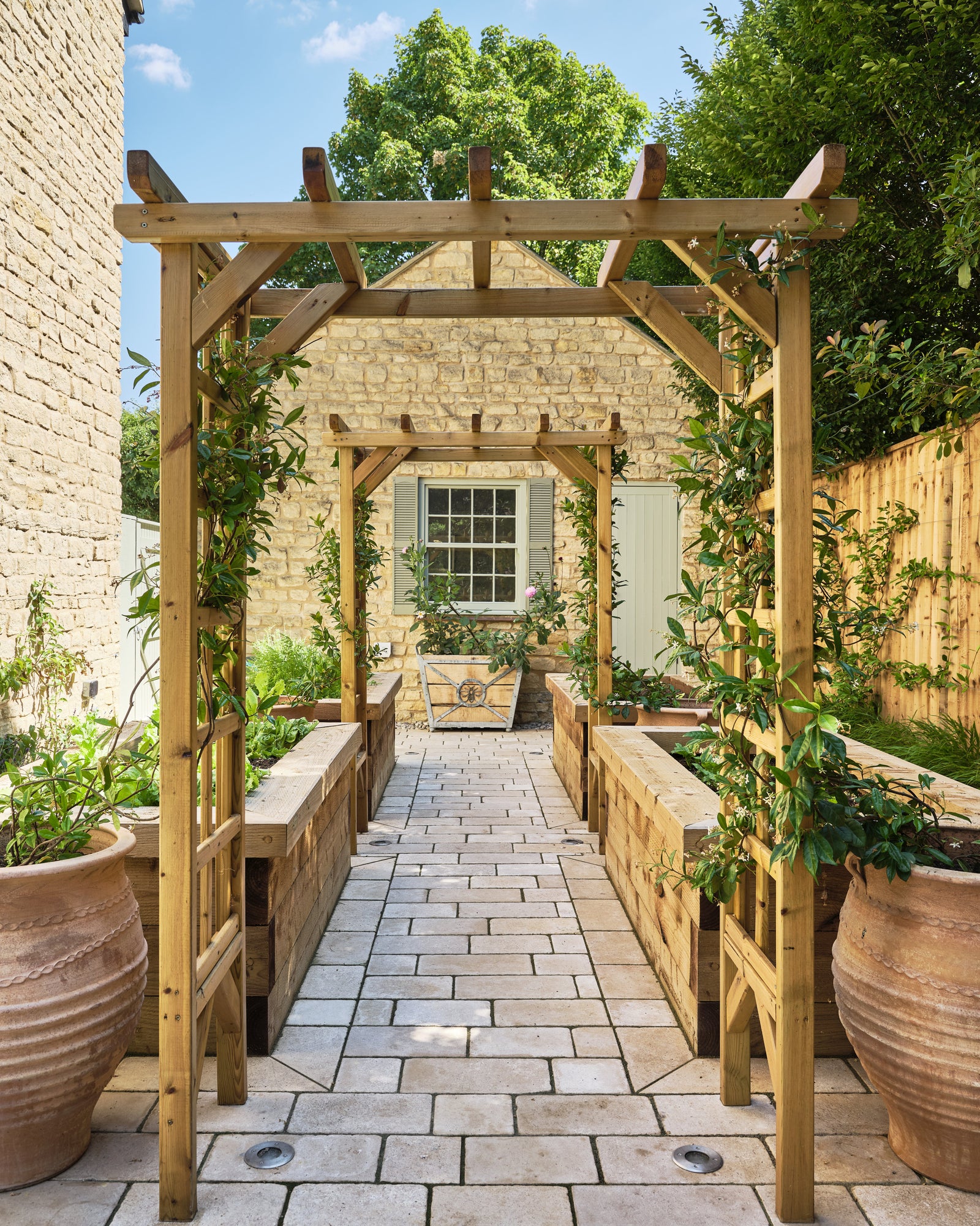 Buscot Limestone Cobble Tumbled & Etched Finish paving a walkway running beneath a timber pergola between raised planters