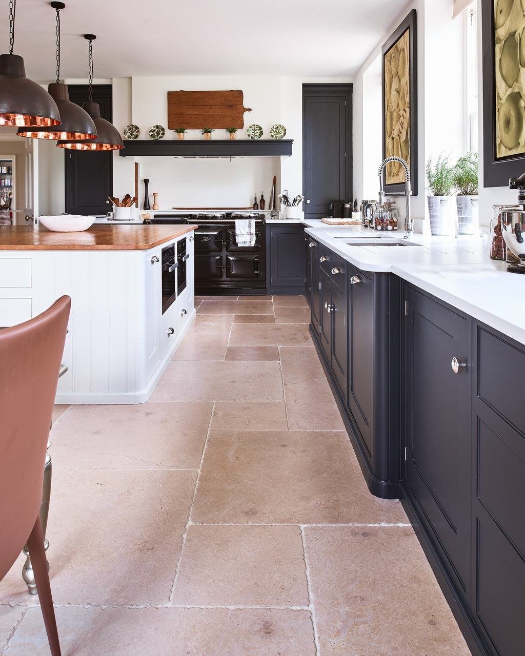 Buscot Limestone Seasoned Finish flagstones running the length of a country kitchen with charcoal cabinetry, a black range cooker and copper pendant lights