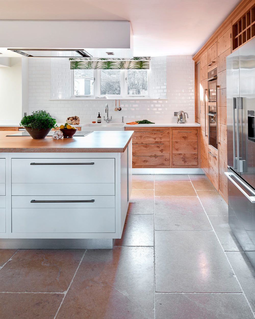 Buscot Limestone Seasoned Finish flooring in a contemporary kitchen with a pale island, burr oak cabinetry and a white metro tiled wall