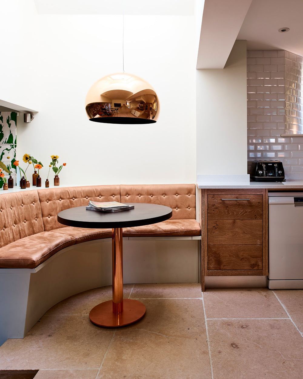 Buscot Limestone Seasoned Finish flooring beneath a curved tan leather banquette and round cafe table lit by a copper dome pendant