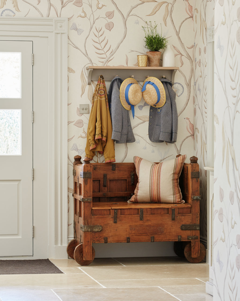 Buscot Limestone Seasoned Finish flooring in an entrance hall with an antique wheeled chest bench, coat hooks and trailing floral wallpaper