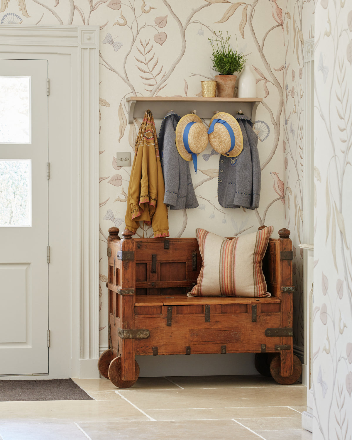 Buscot Limestone Seasoned Finish flooring in an entrance hall with an antique wheeled chest bench, coat hooks and trailing floral wallpaper