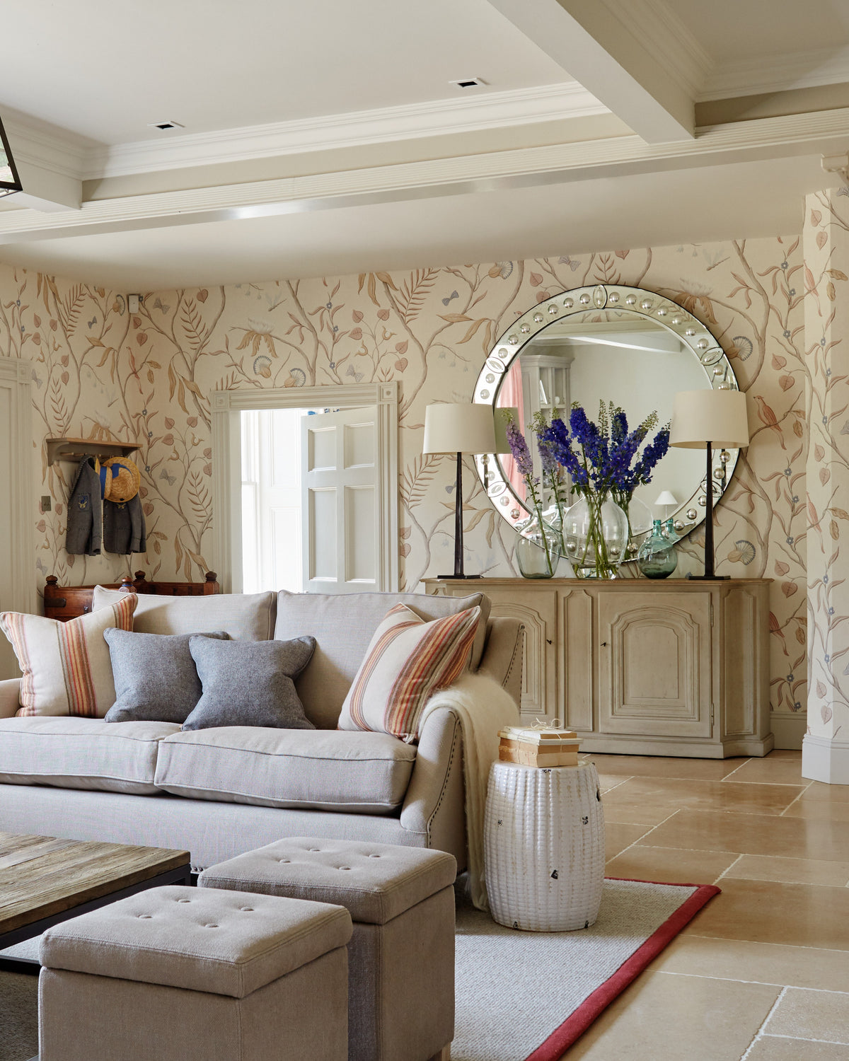 Buscot Limestone Seasoned Finish flooring in a drawing room with linen sofas, a round Venetian mirror and hand painted botanical wallpaper
