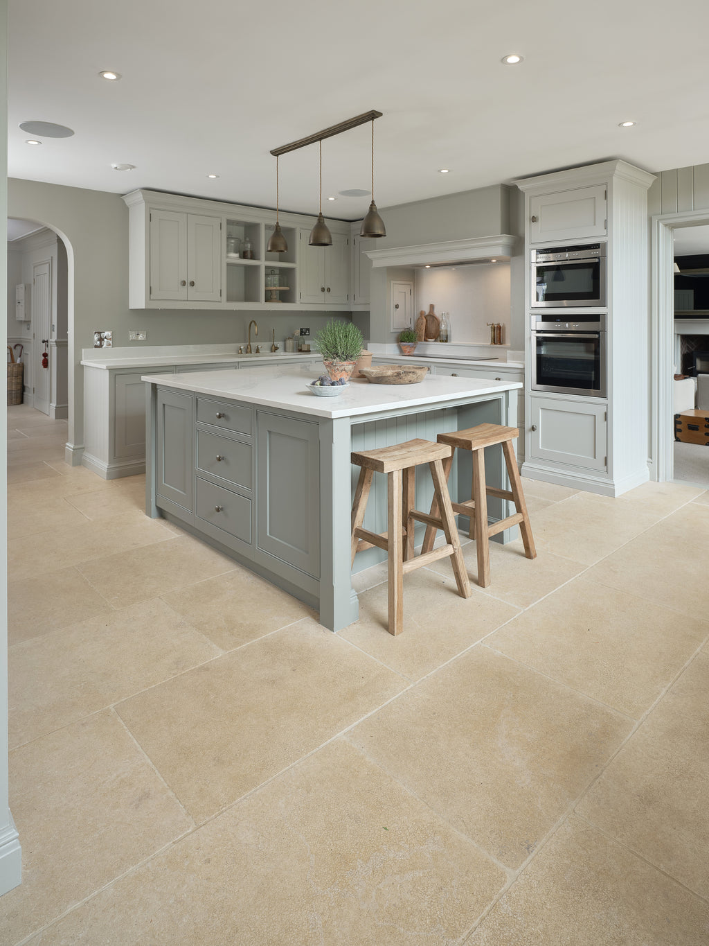Buscot Limestone Tumbled & Etched flagstone floor in an open-plan kitchen with a sage green island and oak stools