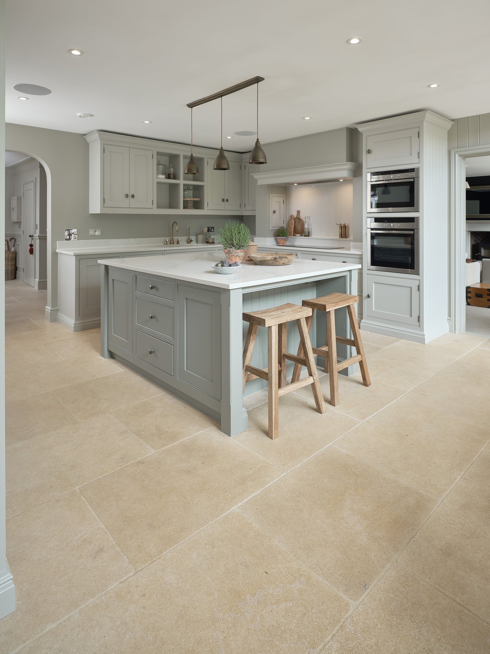 Buscot Limestone Tumbled & Etched flagstone floor in an open-plan kitchen with a sage green island and oak stools