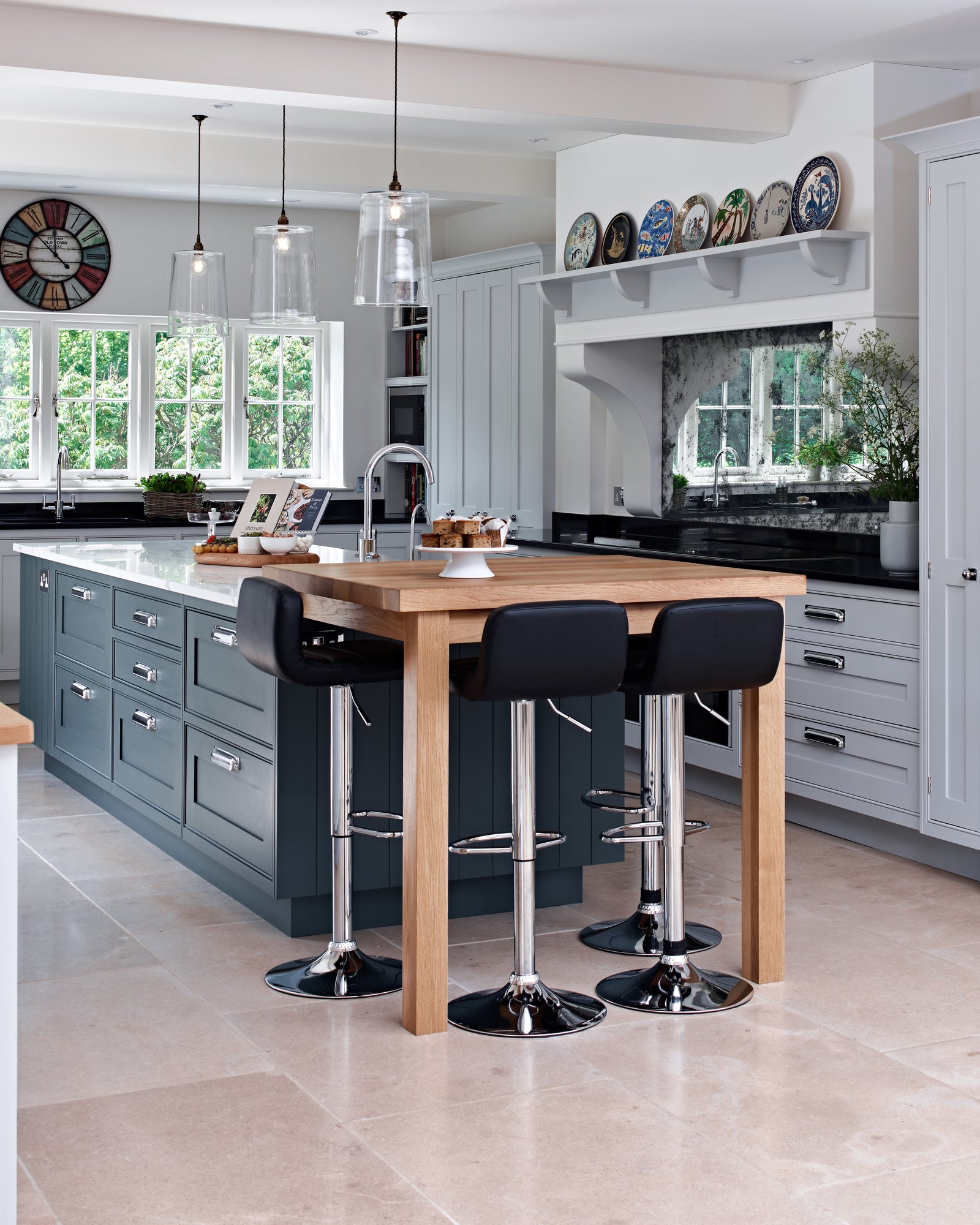 Buscot Limestone Tumbled Finish flooring in a large family kitchen with a dark blue island, oak breakfast table and glass pendant lights