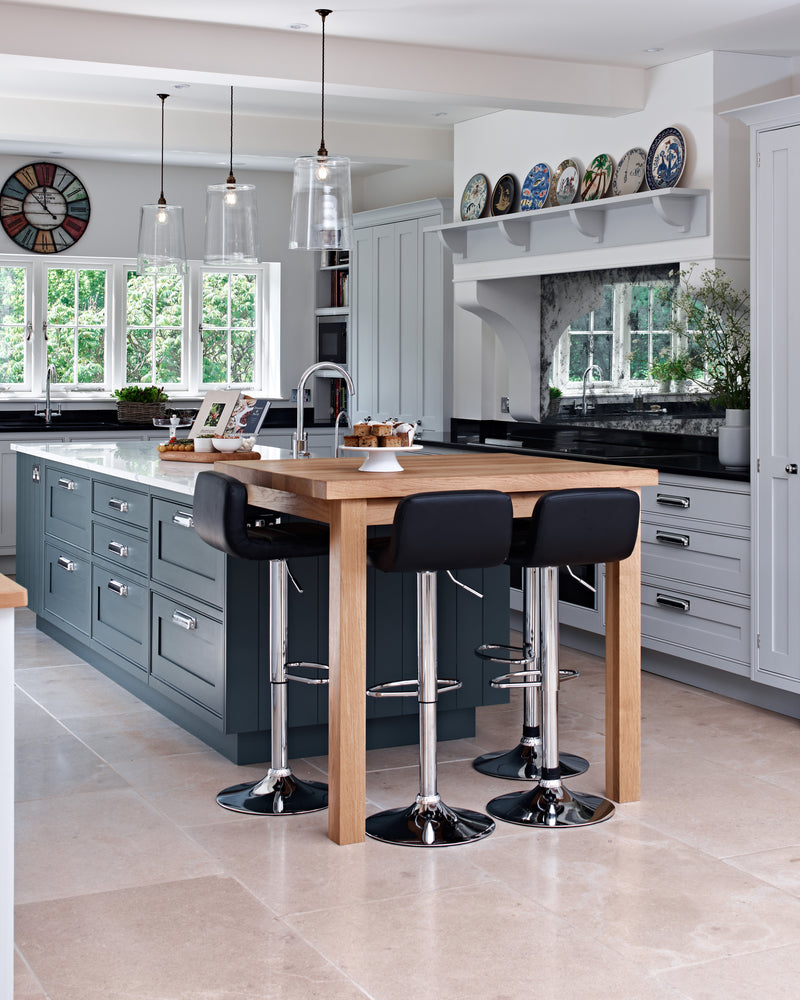Buscot Limestone Tumbled Finish flooring in a large family kitchen with a dark blue island, oak breakfast table and glass pendant lights