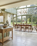 Buscot Limestone Tumbled Finish flooring running from a sage-green kitchen into a glazed conservatory dining room with a wrought chandelier and garden views