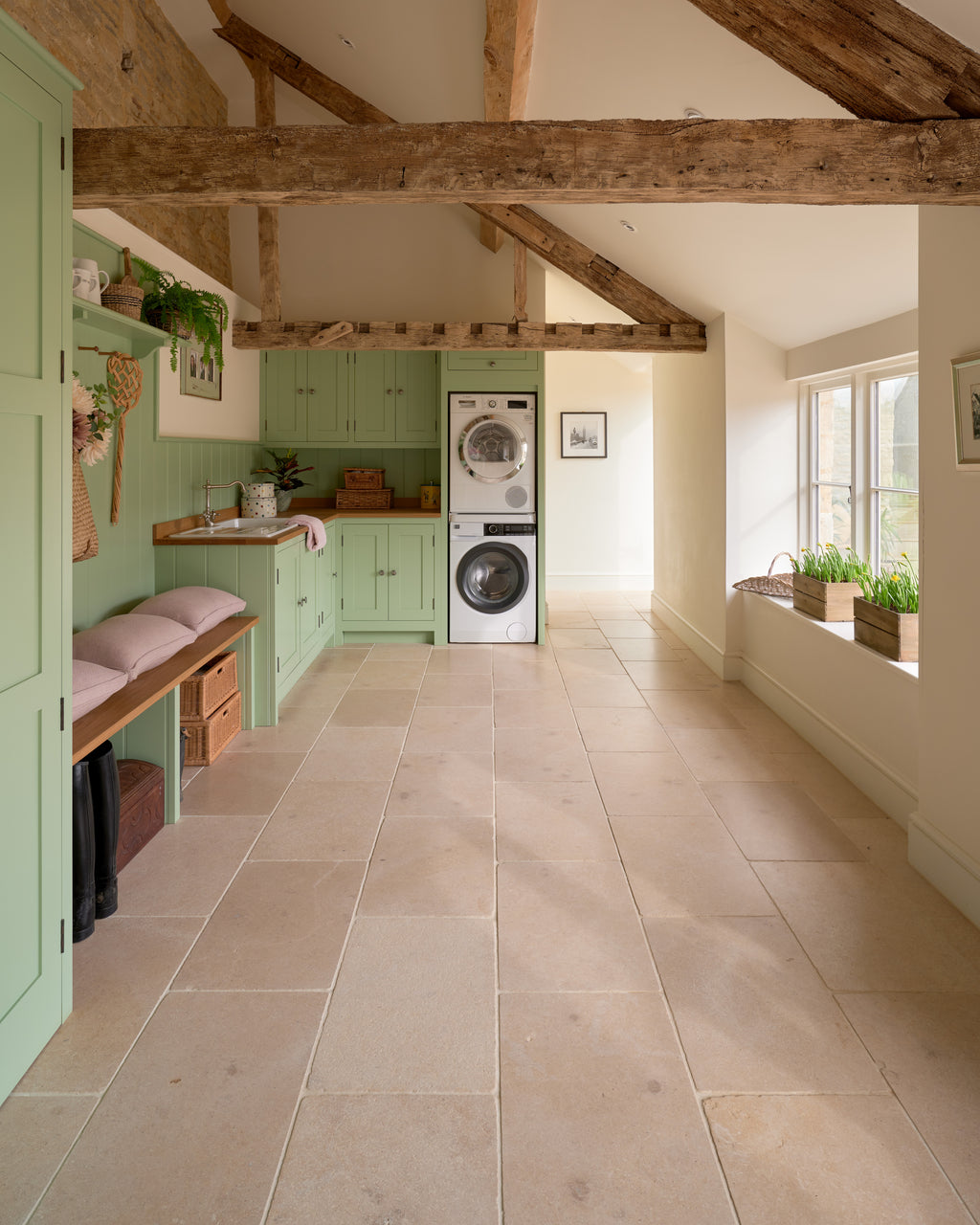 Buscot Limestone Tumbled Finish flooring through a sage-green beamed boot room with a stacked washer and dryer and a cushioned bench