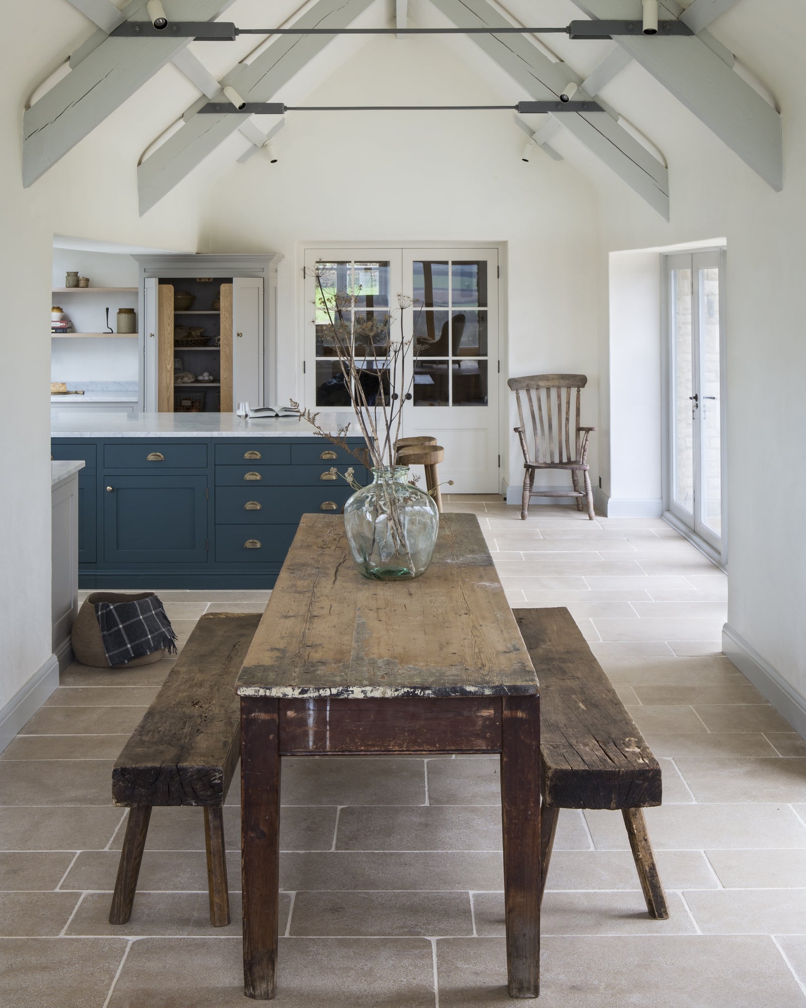 Buscot Limestone Tumbled Finish flooring beneath a reclaimed wood table and benches in a vaulted barn dining room