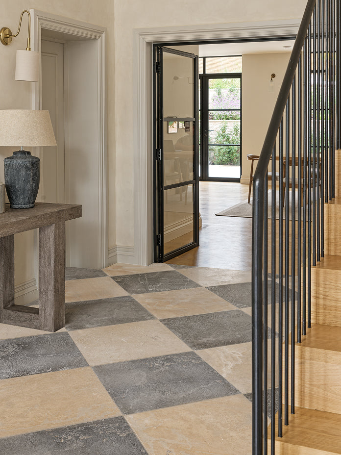 Grey and cream chequerboard stone floor in an entrance hall with an oak staircase and Crittall doors