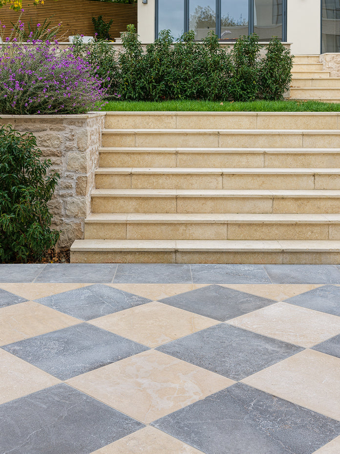 Grey and cream chequerboard paving on a terrace below wide stone steps and planted borders