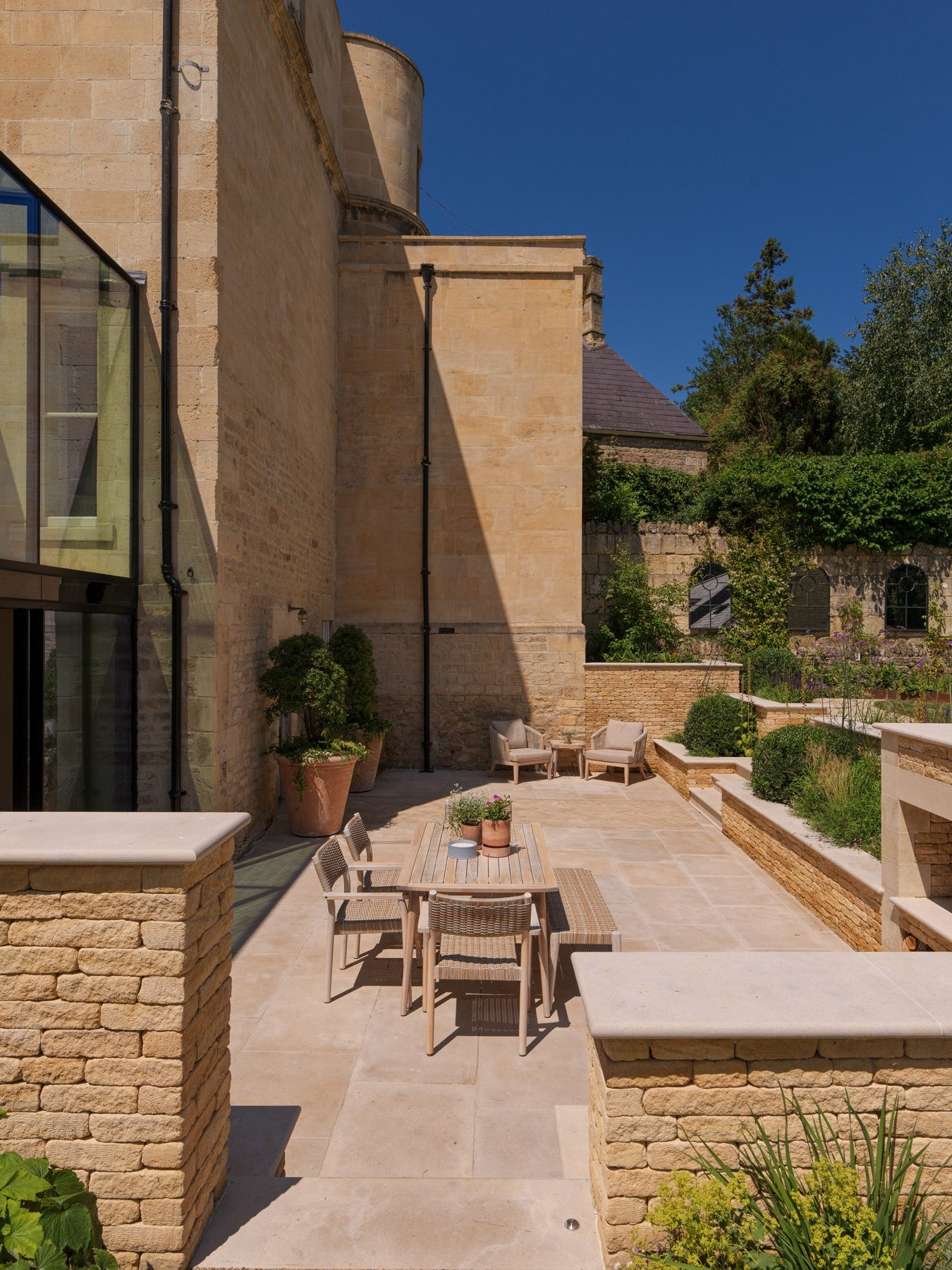 Buscot Limestone Tumbled & Etched paving in a sunlit courtyard dining terrace with dry stone retaining walls