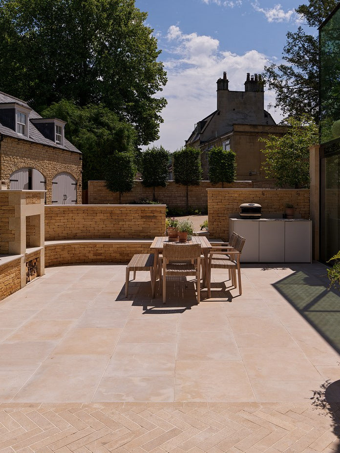 Buscot Limestone Tumbled & Etched paving in a walled courtyard with an outdoor kitchen and pleached trees