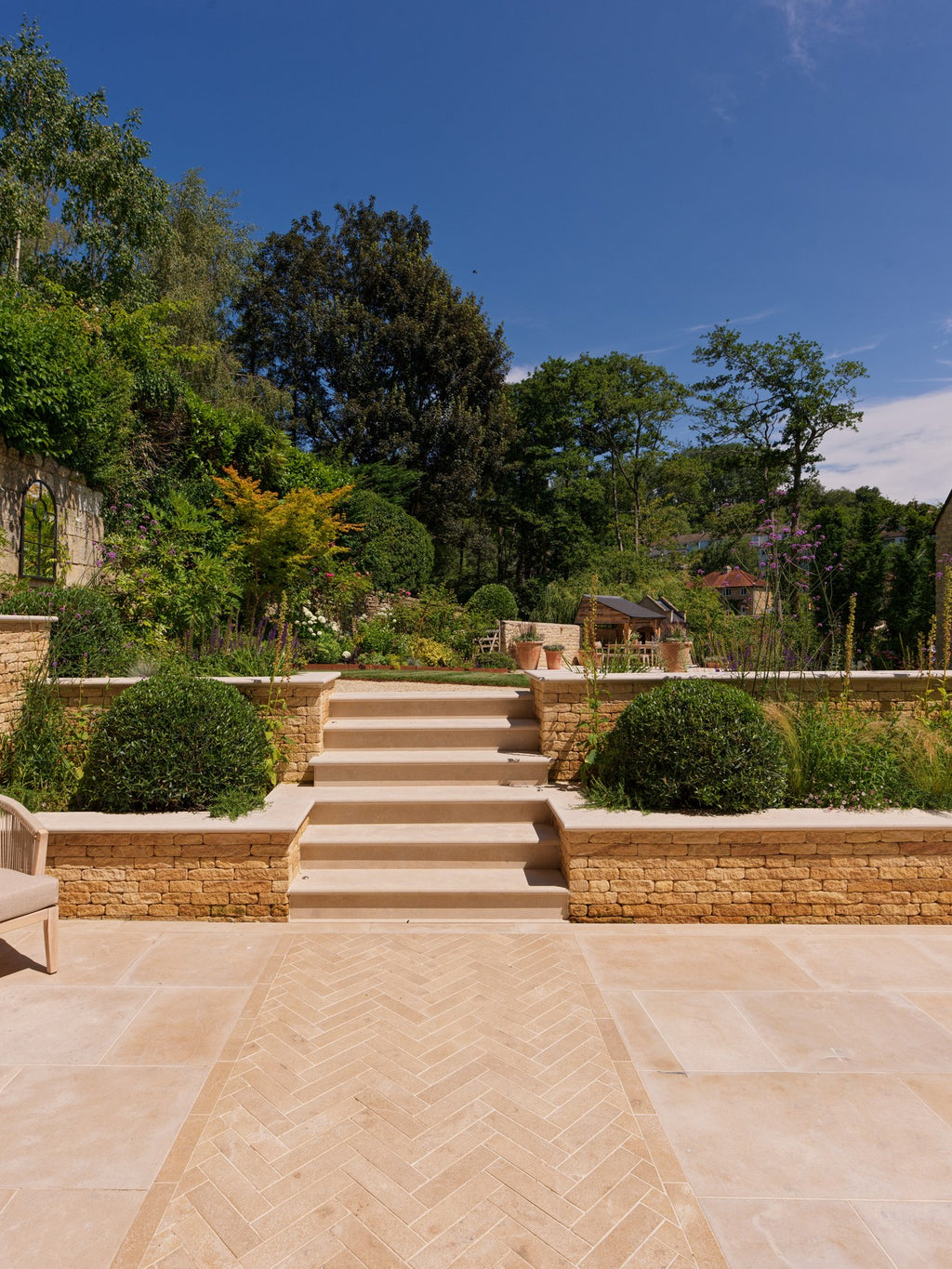 Buscot Limestone Tumbled & Etched terrace with a herringbone runner leading to stone steps and a terraced garden