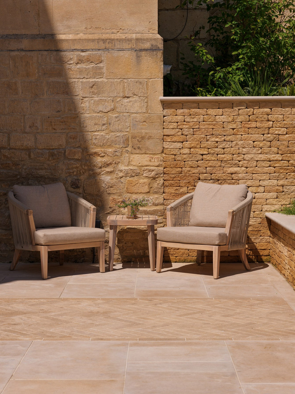 Buscot Limestone Tumbled & Etched paving with a herringbone inset and two rope lounge chairs against warm stonework