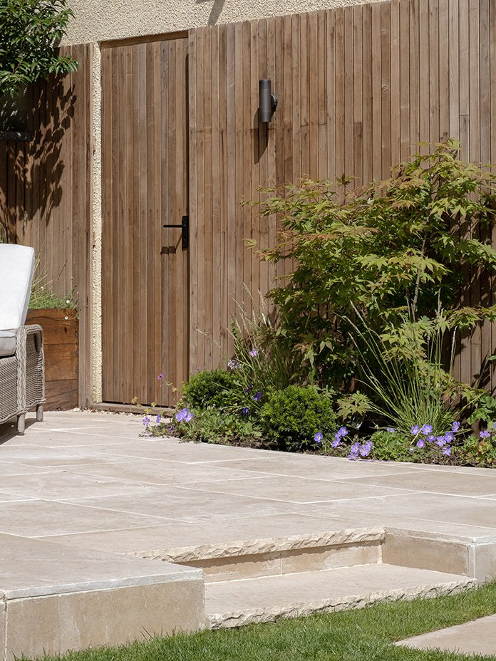 Buscot Limestone Tumbled & Etched paving with riven-edge steps beside a timber gate and geranium planting