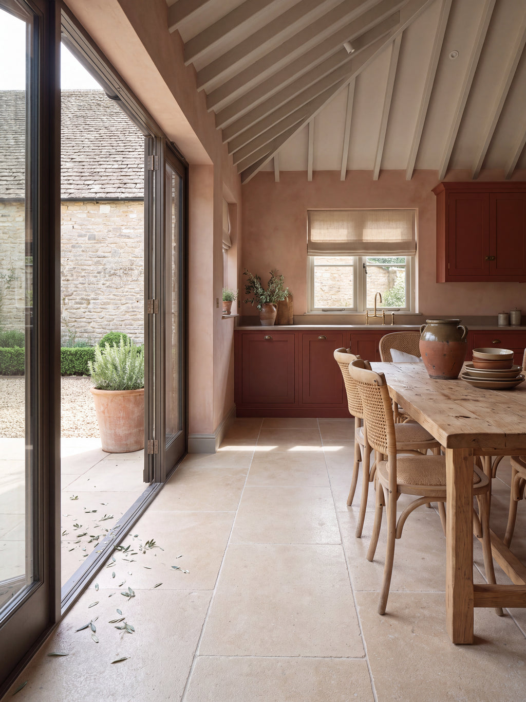Buscot Limestone Tumbled & Etched flagstone floor in a vaulted kitchen with plaster pink walls, deep red cabinetry and bifold doors open to a Cotswold courtyard