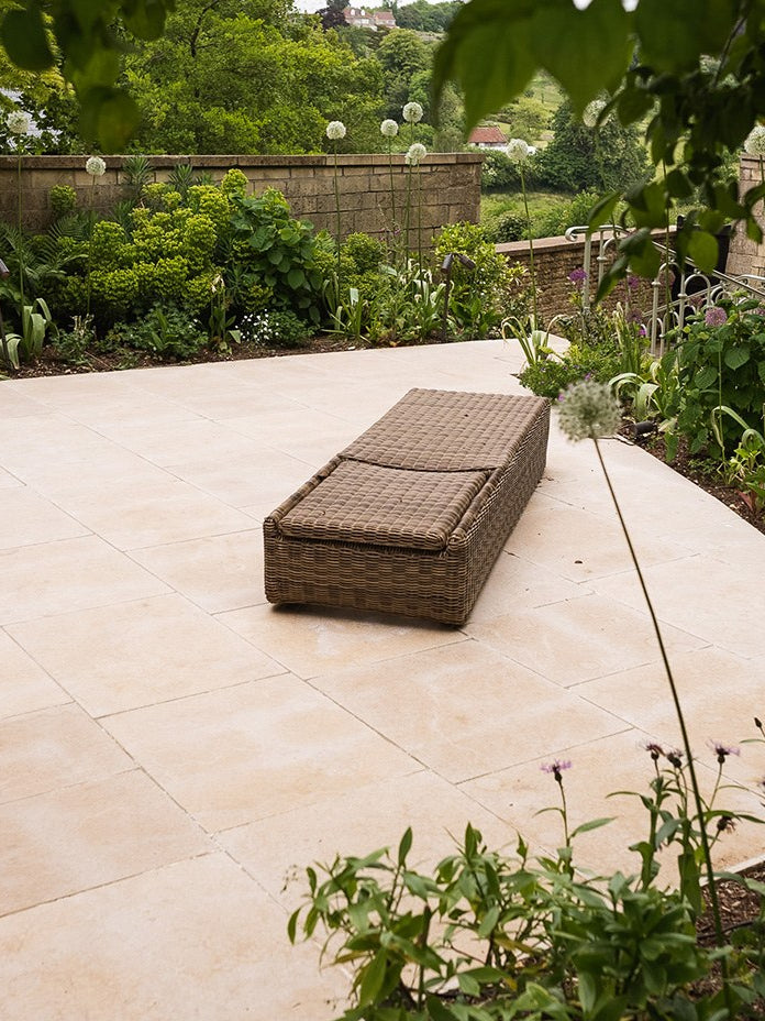 Buscot Limestone Tumbled & Etched terrace with a woven daybed and planted borders looking out to open countryside