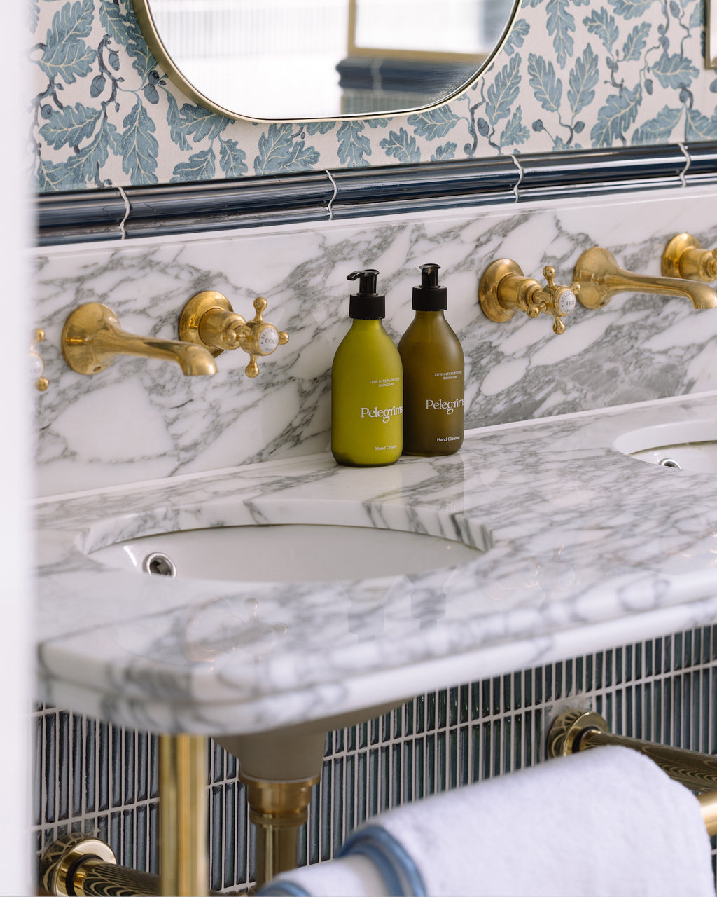 Calacatta Marble Slab as a vanity top and splashback with wall-mounted brass taps, beneath a blue pencil tile trim and oak leaf wallpaper