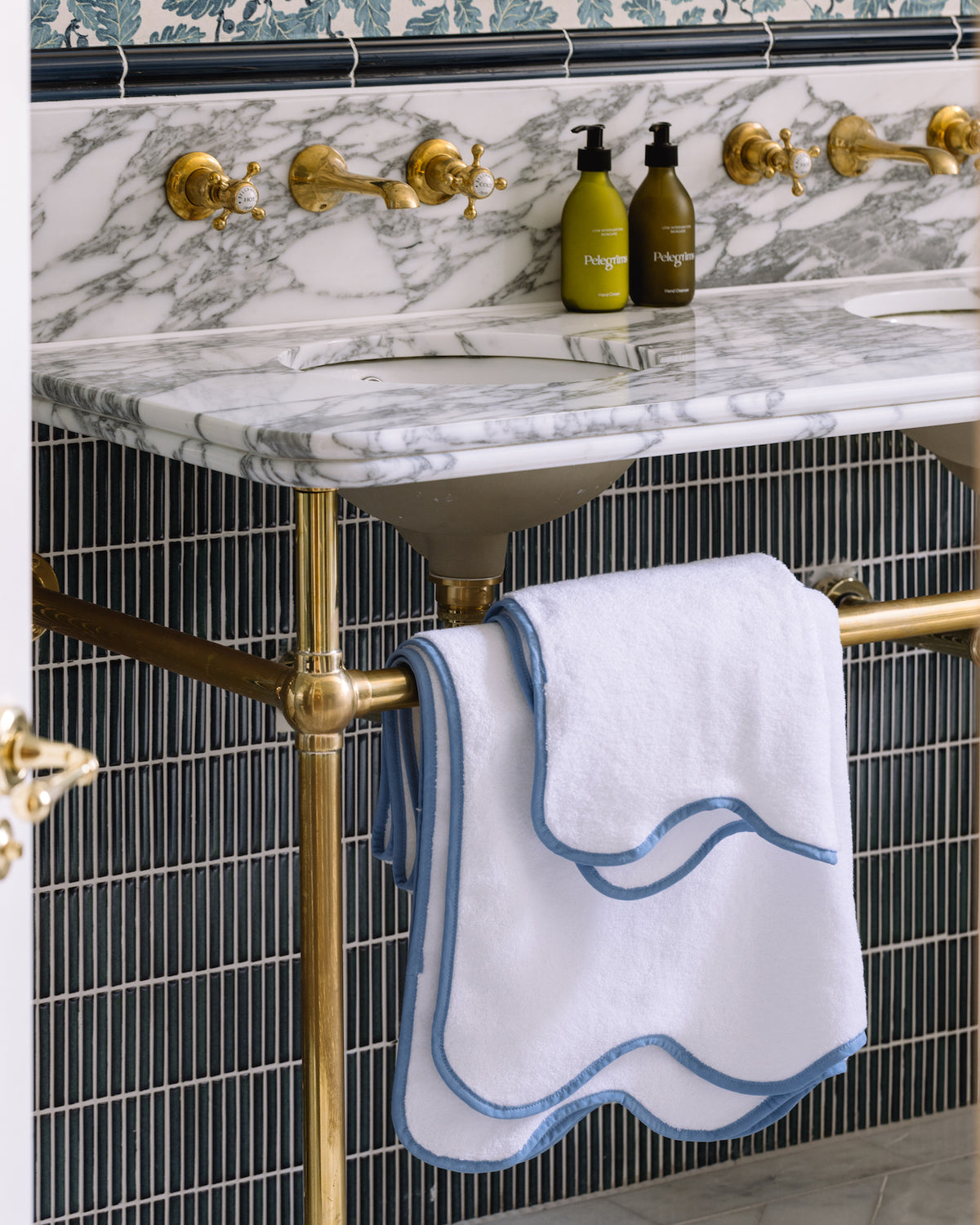 Calacatta Marble Slab forming a double washstand top on a brass frame above dark blue fluted tiling, with scalloped towels on the rail