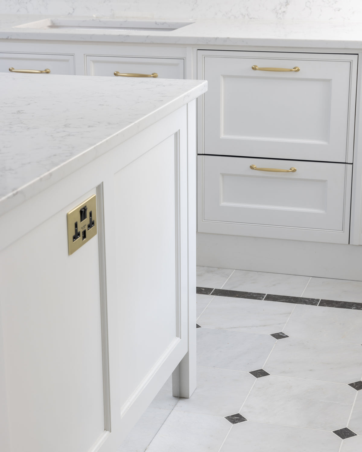 Carrara C Marble Slab as a kitchen island worktop with a bullnose edge, above a pale marble floor laid with dark cabochon insets