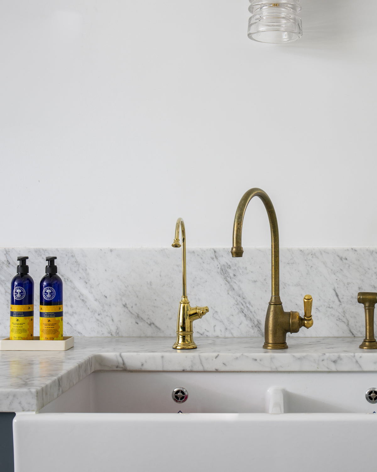 Carrara C Marble Slab as a kitchen worktop and splashback behind a double butler sink, with aged brass taps against exposed brick beyond