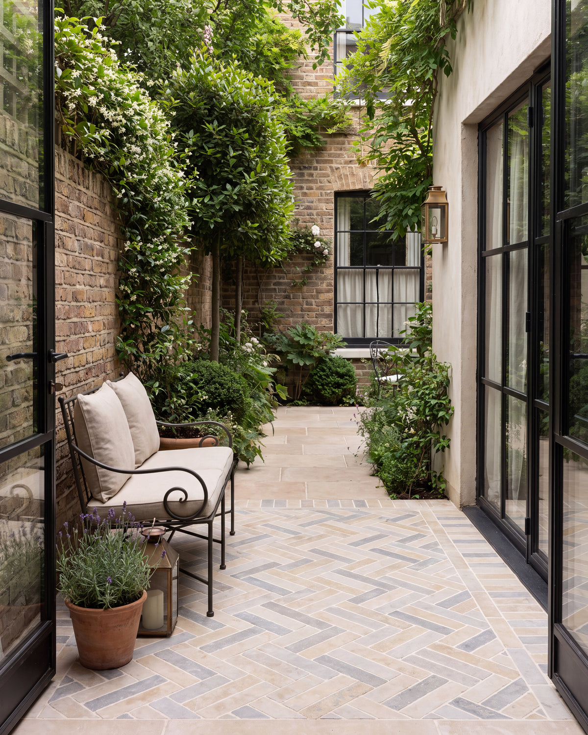 Castilan Limestone Parquet Tumbled laid in herringbone across a narrow London courtyard with jasmine on the brick walls and Crittall doors on both sides