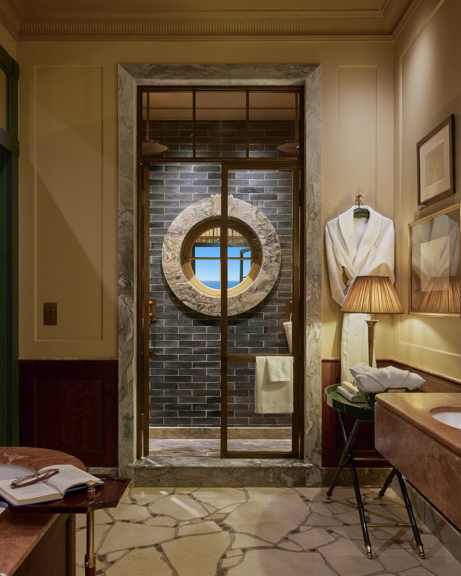 Coral Reef Quartzite Slab framing the shower doorway and porthole window in a coastal bathroom, alongside Buscot Pietra Pazza flooring, Foundry Novo Navy brick tiles and a Versailles Rouge vanity top