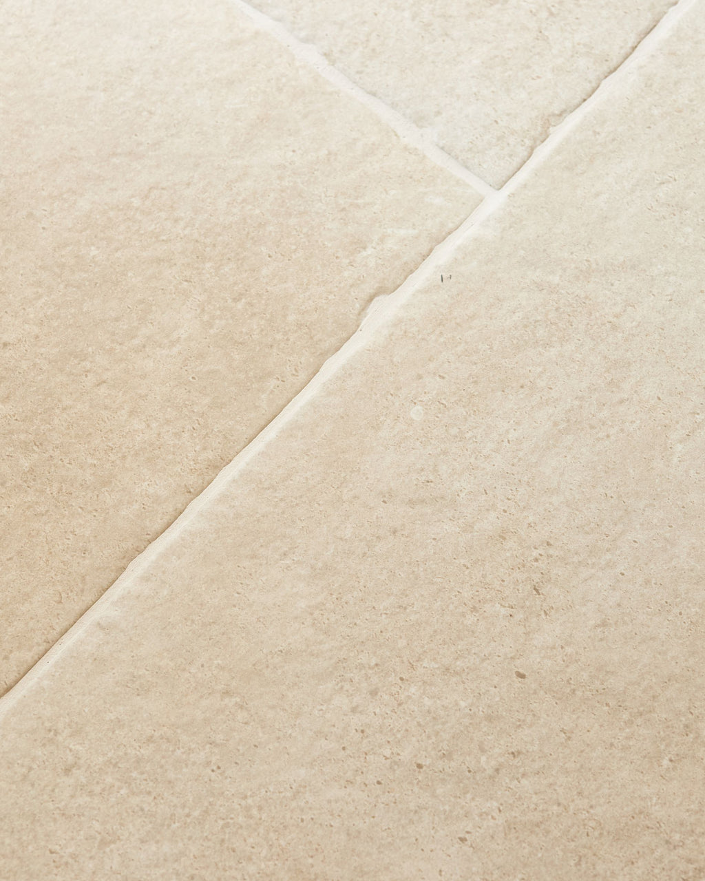 Cotswold Porcelain Matt in close detail, a long diagonal grout joint running between two tiles with fine speckling across the warm cream surface