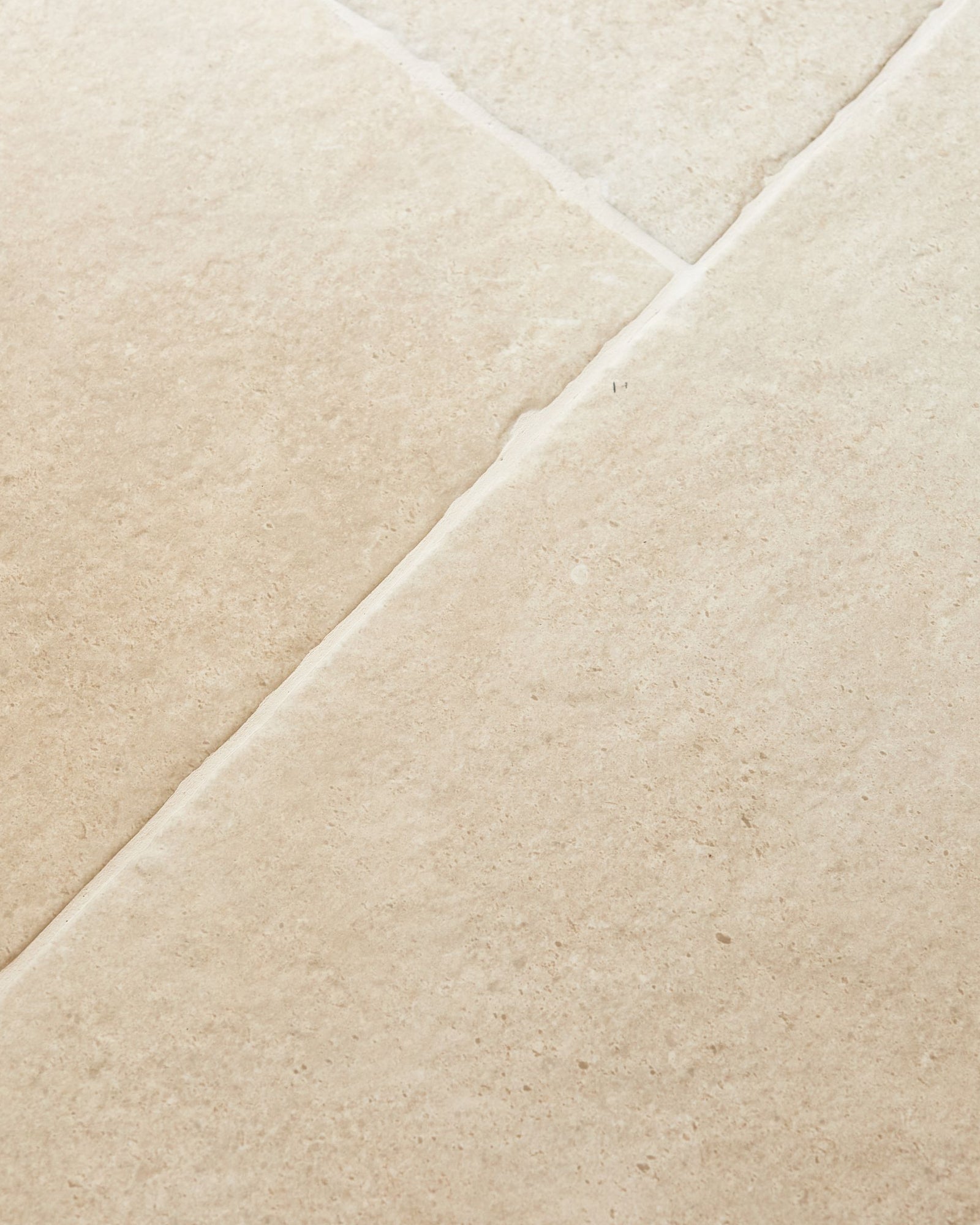 Cotswold Porcelain Matt in close detail, a long diagonal grout joint running between two tiles with fine speckling across the warm cream surface